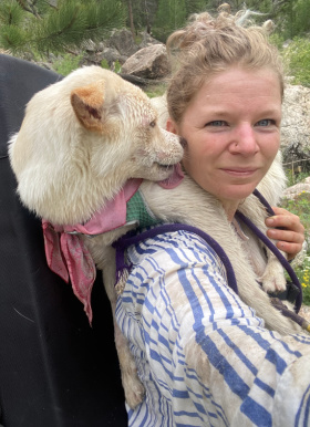 Amy Christensen with a white dog on her back licking her cheek