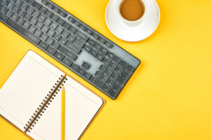 computer keyboard, cup of coffee, notebook, and pencil on yellow background