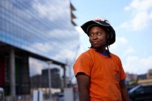 Construction worker Brittney A. Wallace stands in front of the Neuroscience Research Building in an orange shirt and hard hat