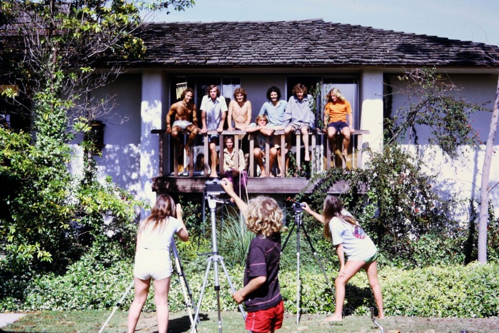 Paul Bridgman, Vance Lemmon, Dan Bridgman, Rusty Preisendorfer, and friends leaning on the balcony of the Starlight Drive home as three people take photographs