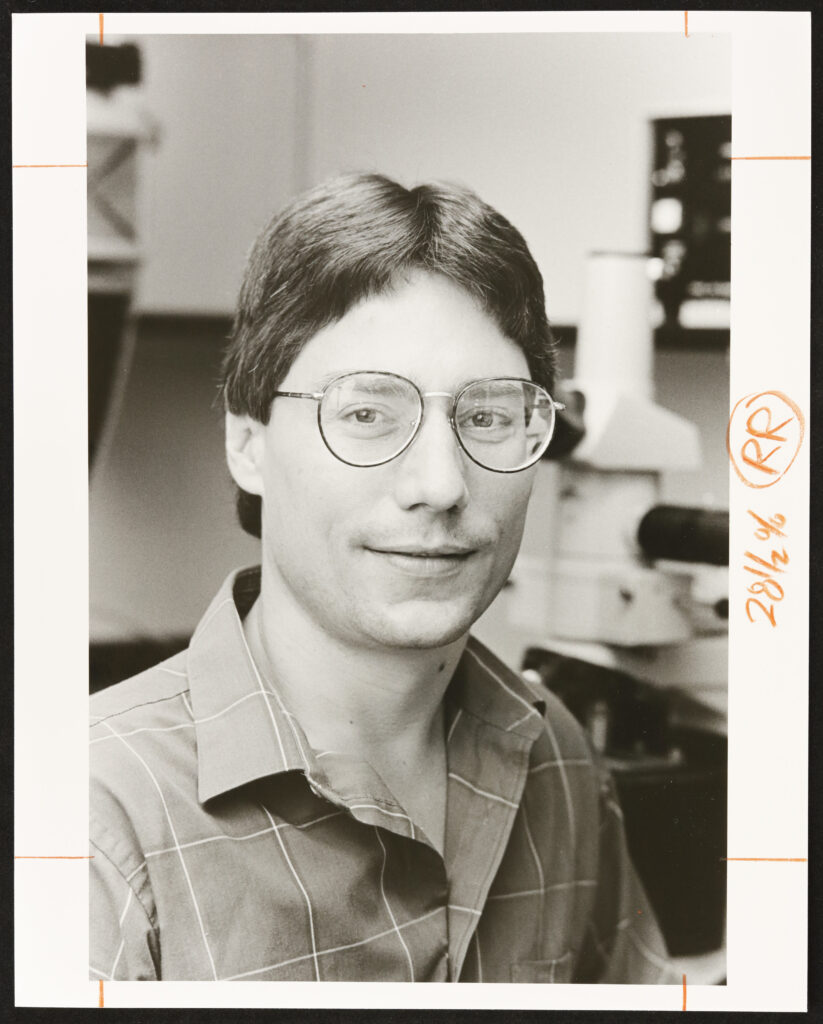 Dennis O'Leary as a faculty member in the 1980s at WashU. Photo is black and white. He has short hair and is wearing glasses with a collared shirt.