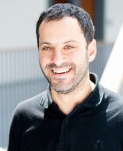 Mazen Kheirbek is a man with short hair and is wearing a black polo shirt and smiling.