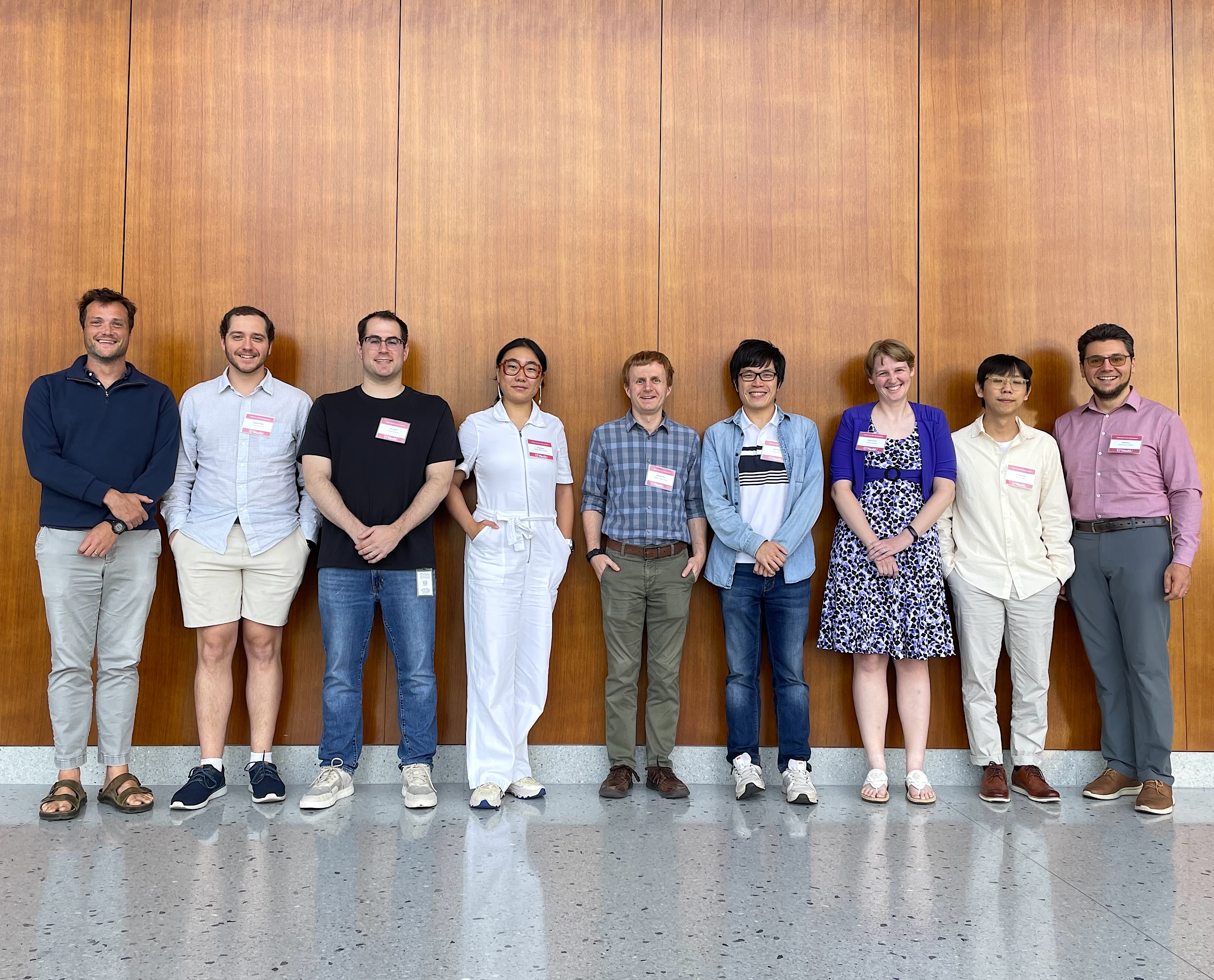 The nine guest speakers of the 2025 CNNG line up single file in front of a brown wall.
