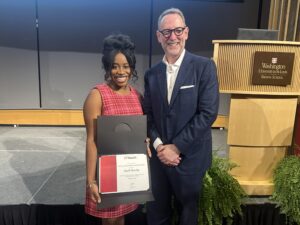 Kia Barclay poses with her Provost’s Graduate Student Research Excellence Award. She is smiling and wearing a red dress. Provost Mark D. West stands next to her.
