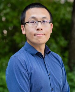 Shuo Wang is a man with short dark hair and wearing glasses and a blue shirt.