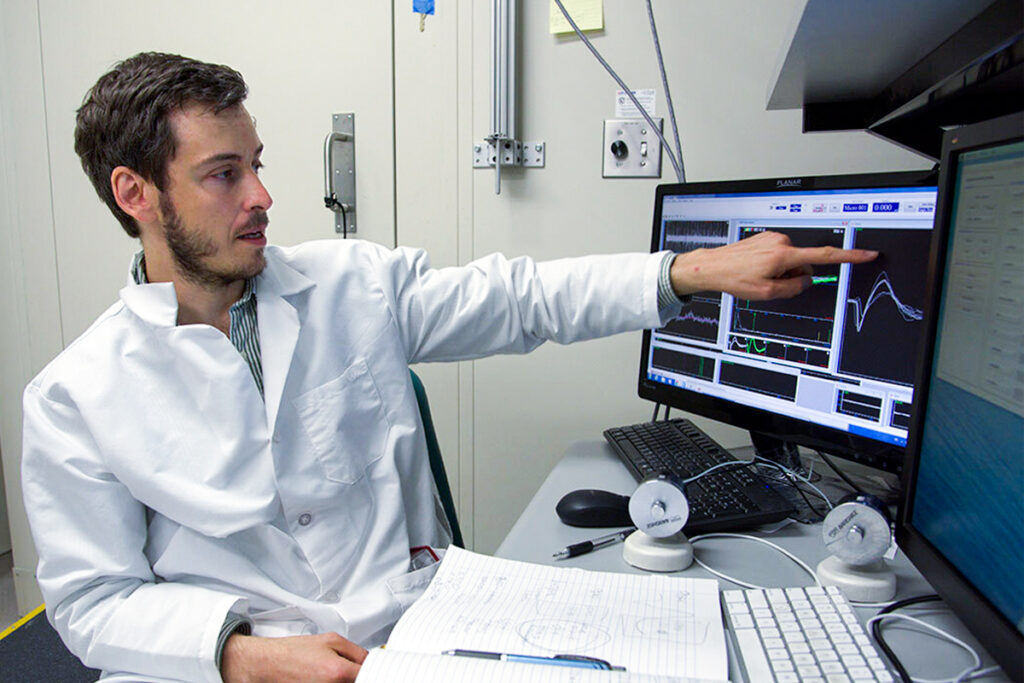 Scientist Ilya Monosov wearing a white lab coat points to a computer screen