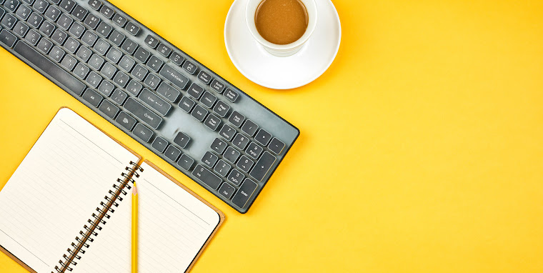 computer keyboard, cup of coffee, notebook, and pencil on yellow background
