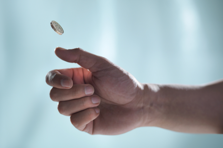 A hand flipping a gold coin on a blue background