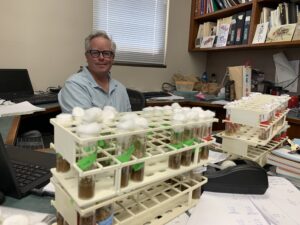 Paul Shaw sitting at his desk behind a rack of fruit fly tubes